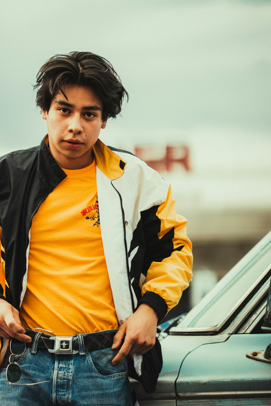 a young man standing next to a parked car